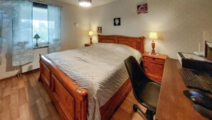 A bedroom with a wooden bed, a desk with a chair, and two bedside lamps.