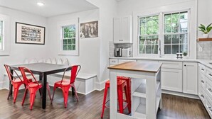 A modern kitchen with white cabinetry, a wooden countertop, and red chairs.