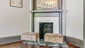 A room with a fireplace, two ottomans, a map on the wall, and a chandelier above the fireplace.