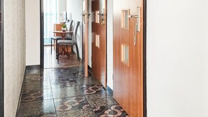 A hallway with patterned floor tiles, a wooden door with a handle, and a dining area with a table and chairs in the background. - 3 bedroom lovely apartment in Wiselka (Wiselka)