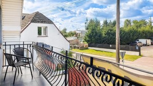 A balcony with a curved black metal railing, two wicker chairs, and a view of a white house with a red roof and a small window. - 3 bedroom lovely apartment in Wiselka (Wiselka)