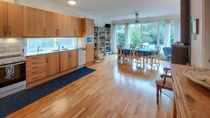 Eine moderne Küche mit Holzausstattung, ein Essbereich mit Tisch und Stühlen sowie ein großes Fenster mit Blick ins Freie.