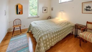 Ein Schlafzimmer mit einem Bett, zwei Stühlen, einem kleinen Tisch, einem Fenster und einem Spiegel.