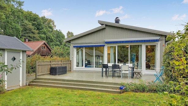 Ein modernes Haus mit überdachter Terrasse, großen Fenstern und einem kleinen Garten.