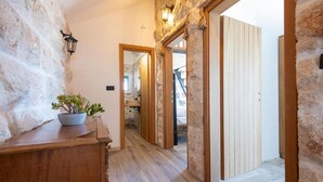 Un couloir aux murs en pierre, au plancher en bois, et sur lequel se trouve une plante en pot posée sur une table en bois.
