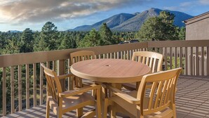 Eine Holzterrasse mit rundem Tisch und Stühlen, mit Blick auf eine Berglandschaft.