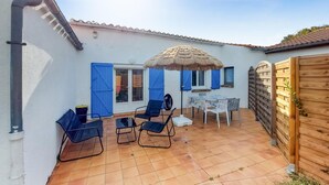 Um pátio com piso de azulejos, uma mesa com cadeiras, uma porta azul e uma cerca de madeira.