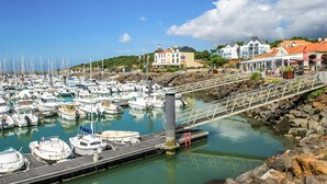 Uma marina com vários barcos atracados, um cais de pedra e edifícios ao fundo.