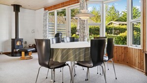 A dining area with a table and chairs, a wood-burning stove, and large windows with a view of greenery. - 3 bedroom gorgeous home in Malling (Malling)