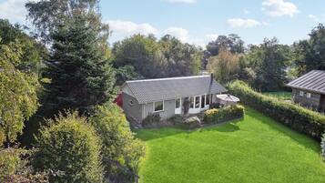 A single-story house with a sloped roof, surrounded by a well-maintained lawn and dense trees.