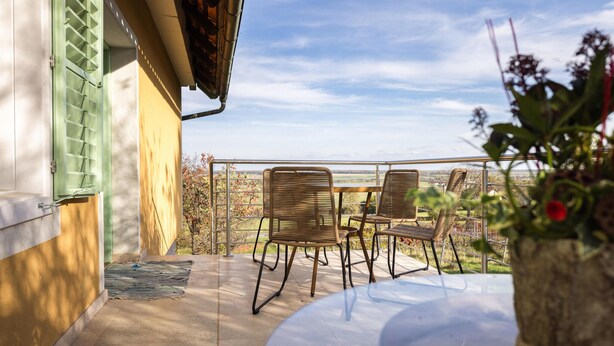 A balcony with wicker chairs and a table, overlooking a scenic landscape.