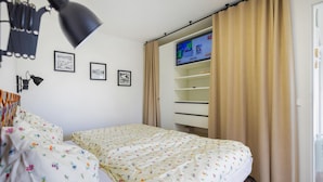 A bedroom with a bed, a TV mounted on the wall, a wardrobe, and a desk lamp.