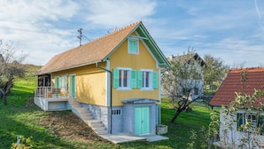 A two-story house with a red-tiled roof, green shutters, and a small balcony.