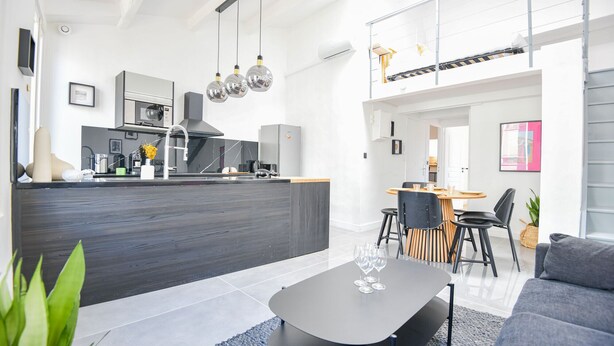 Una cucina moderna con isola centrale, un'area pranzo con tavolo rotondo e un soggiorno con divano e tavolino.