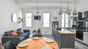 Una cucina moderna con isola centrale, zona pranzo con tavolo rotondo e angolo relax con divano e televisore.