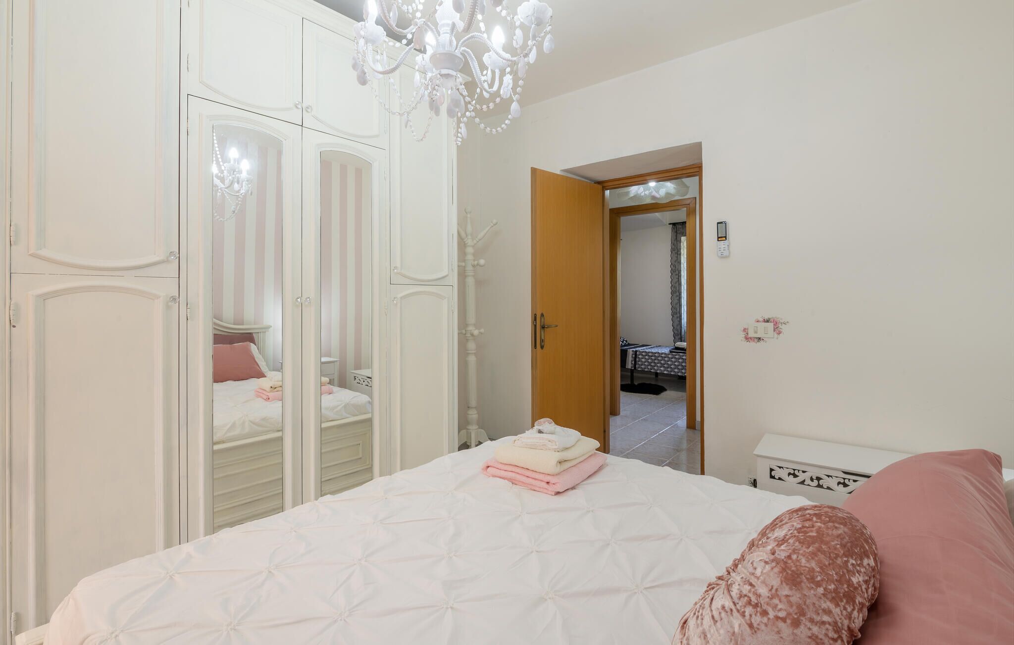 A bedroom with a bed, a wardrobe, a chandelier, and a door leading to another room.
