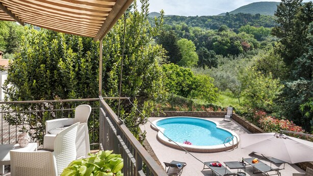A pool area with a view of a lush landscape, surrounded by wicker furniture and a covered seating area.
