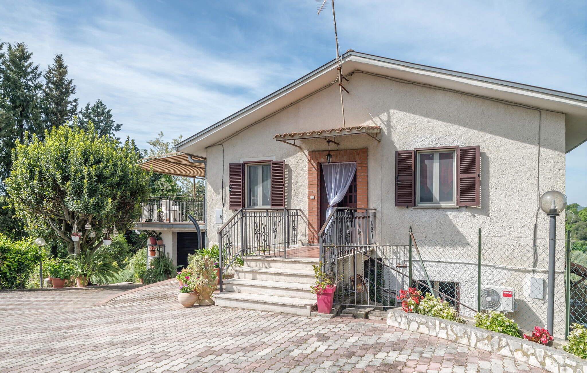 A two-story house with a balcony, potted plants, and a clear sky.