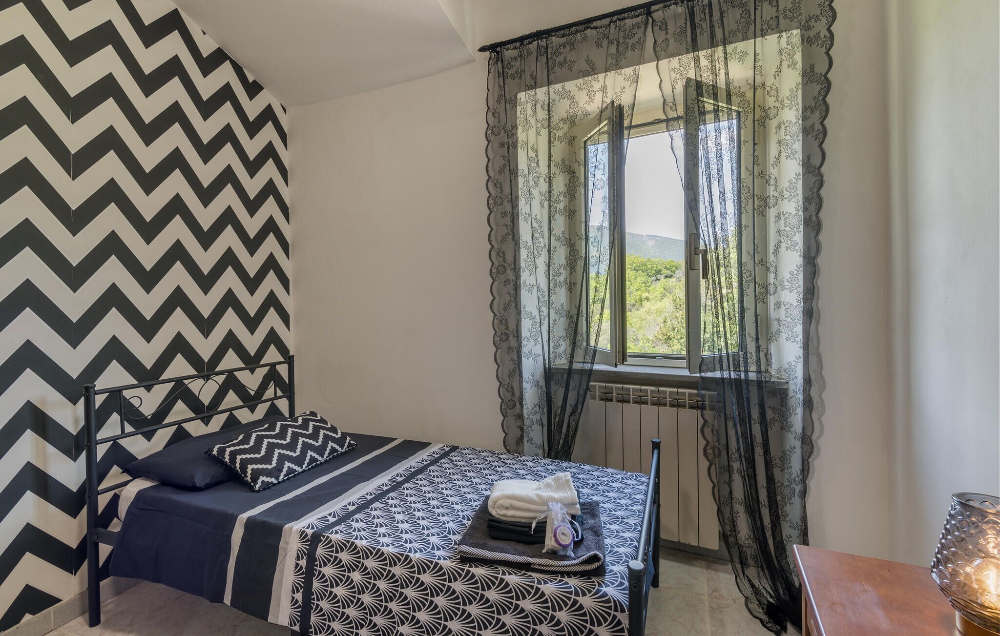 A bedroom with a bed, a radiator, a window with sheer curtains, and a patterned wall.
