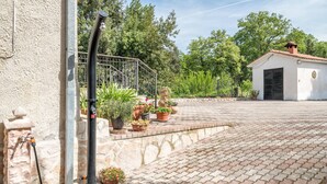 A paved courtyard with potted plants, a metal fence, and a building with a tiled roof.