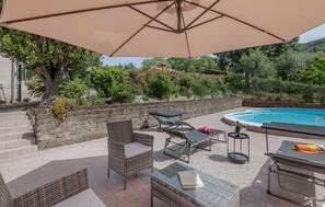 Un espace aménagé au bord de la piscine, avec des chaises longues, une table et un grand parasol.