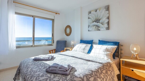 A bedroom with a large bed, a view of the sea, a round mirror, and a painting of a flower. - Cozy apartment in Torrevieja (Torrevieja)