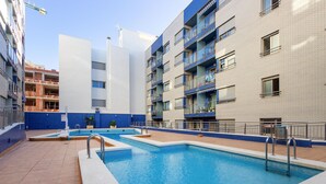A swimming pool area with multiple pools, a blue and white building with balconies, and a clear sky. - Cozy apartment in Torrevieja (Torrevieja)
