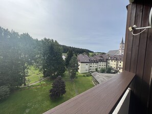 Vista desde un balcón sobre una zona residencial con una torre de iglesia, un parque verde y una hilera de edificios de varios pisos.