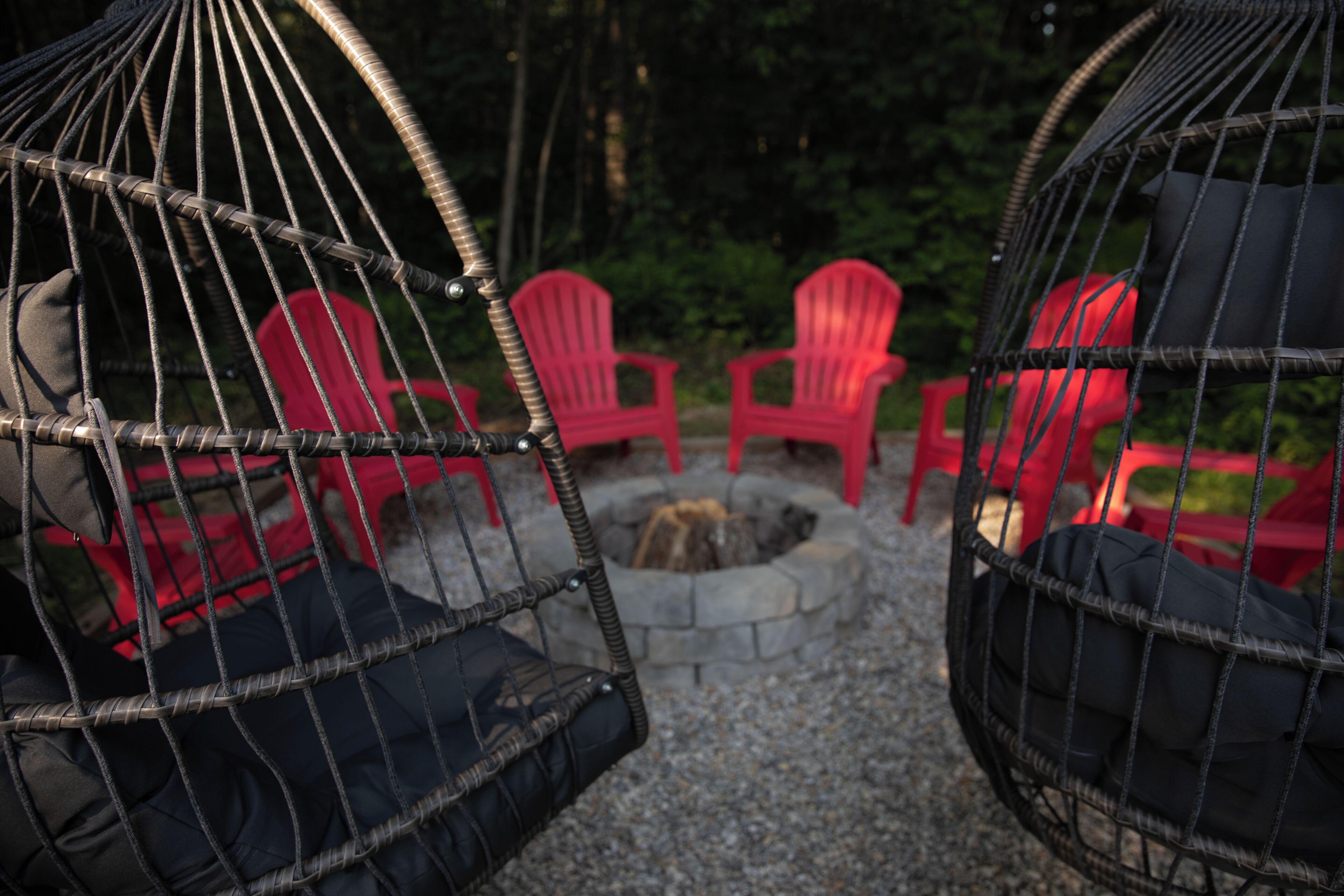 Un sillón hamaca con cojín, un hogar de piedra y sillas rojas.