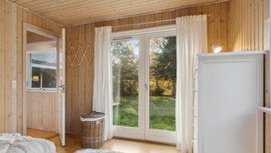 A wooden room with a bed, a wicker basket, and a sliding glass door leading to a garden. - Amazing home in Nykøbing Sj with WiFi (Nykøbing Sj)