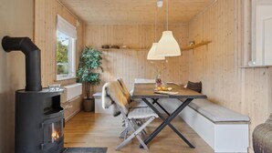 A cozy cabin interior with a wood-burning stove, a dining table with benches, and a hanging light fixture. - Amazing home in Nykøbing Sj with WiFi (Nykøbing Sj)