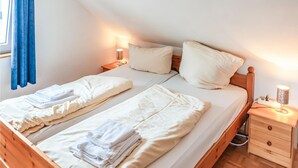 Une chambre double avec deux lits, chacun équipé d’un oreiller et d’une serviette pliée. Il y a une table de chevet avec une lampe et une prise de courant.