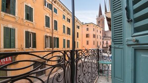 En balkon med udskårne jerngelændere med udsigt over en gade med historiske bygninger, herunder et kirketårn.