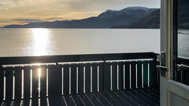 Un balcon offrant une vue sur un lac paisible et des montagnes au coucher du soleil.