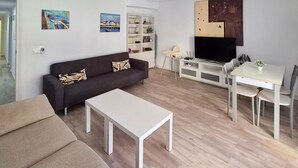 Una sala de estar con sofá, mesa de centro, televisor y un comedor con sillas y mesa.