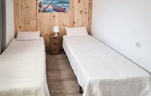 A room with two beds, a wooden wall, a painting, a lamp, and a small wooden dresser.