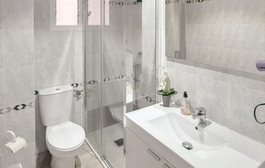 A modern bathroom with a toilet, glass shower enclosure, and a white sink with a mirror above it.