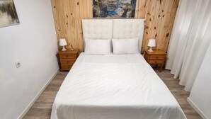 Un dormitorio con una cama grande, dos mesitas de noche con lámparas, paneles de madera en las paredes y un cuadro sobre la cama.