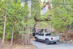 A white pickup truck parked in a forested area with a wooden cabin in the background. - 1 Mi to Lake Arrowhead Village! Cabin w/ Game Room (Lake Arrowhead)