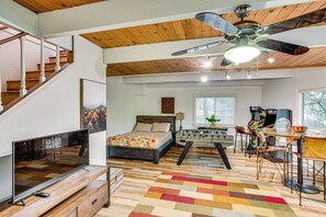 A spacious living area with a wooden ceiling, a large flat-screen TV, a bed with a colorful bedspread, a foosball table, and a foosball table chair. - 1 Mi to Lake Arrowhead Village! Cabin w/ Game Room (Lake Arrowhead)
