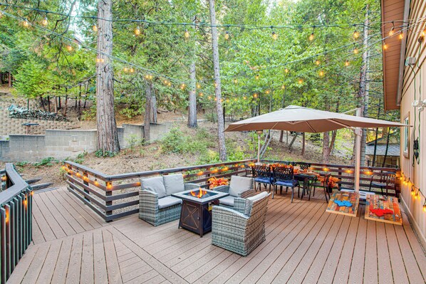 An outdoor deck with wicker furniture, a fire pit, and string lights. - 1 Mi to Lake Arrowhead Village! Cabin w/ Game Room (Lake Arrowhead)