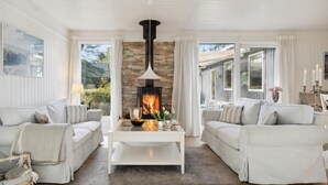 A cozy living room with a fireplace, white furniture, and large windows.