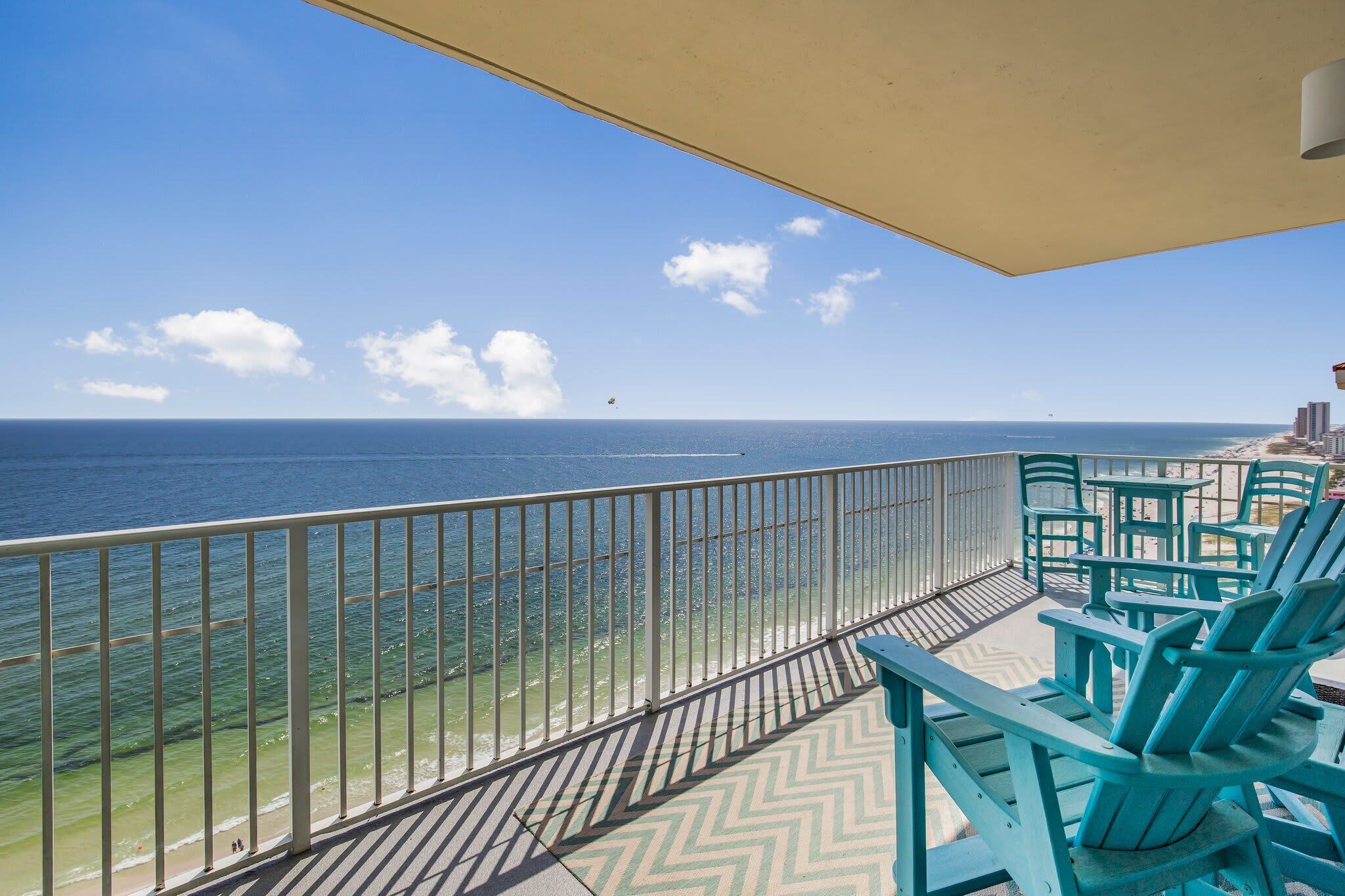 A balcony with a view of the ocean, featuring a railing and several chairs.