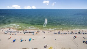 Ein Strand mit Reihen von Sonnenschirmen und Liegestühlen, wolkenlosem Himmel und ruhiger See.