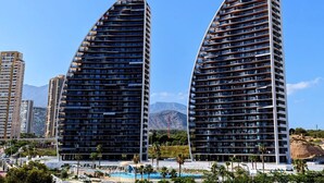 Two modern, curved high-rise buildings with balconies, surrounded by palm trees and a pool area. - SUNSET WAVES WoW apartment (Benidorm)