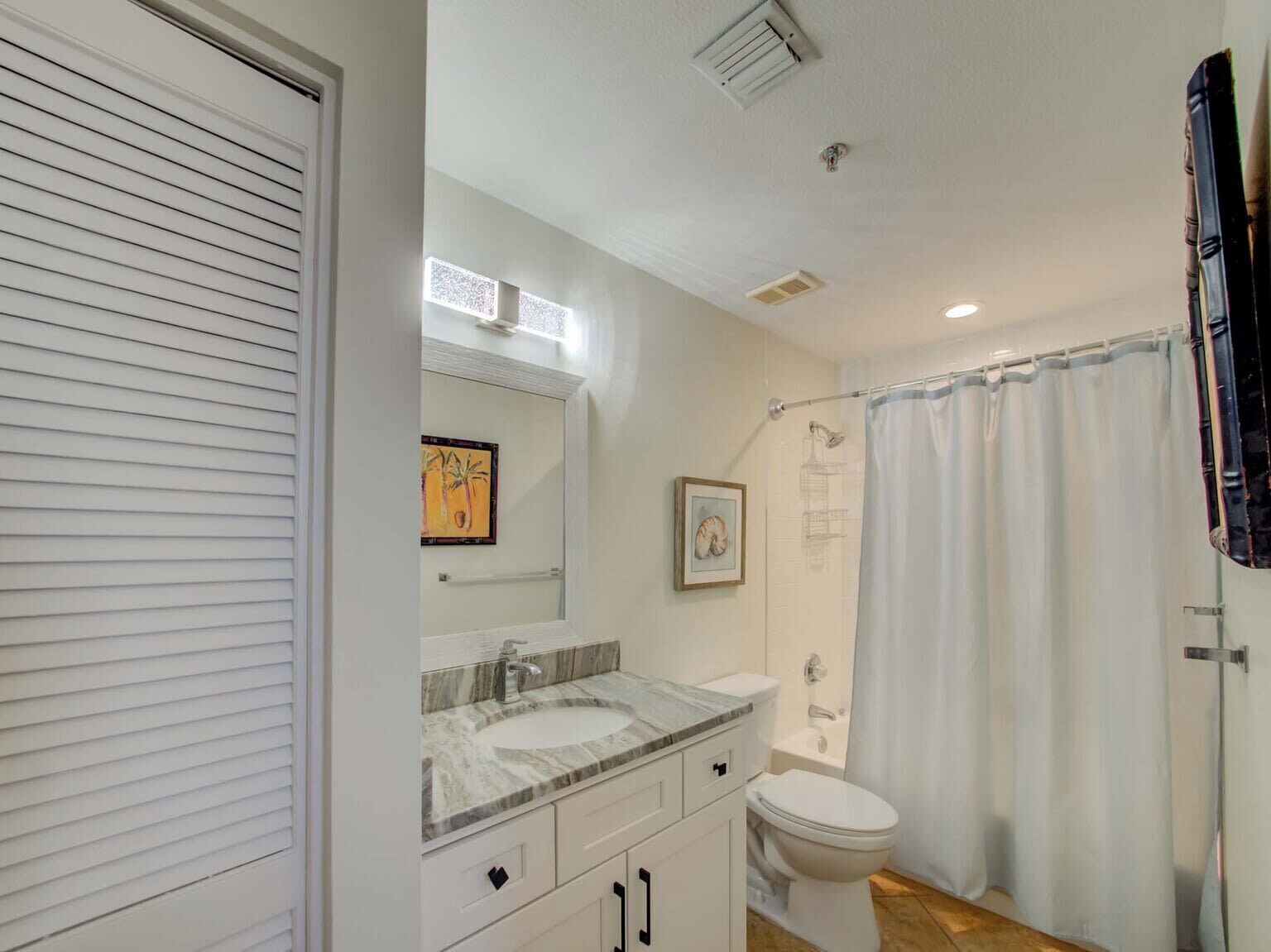 A bathroom with a white vanity, a sink, a toilet, and a shower curtain.