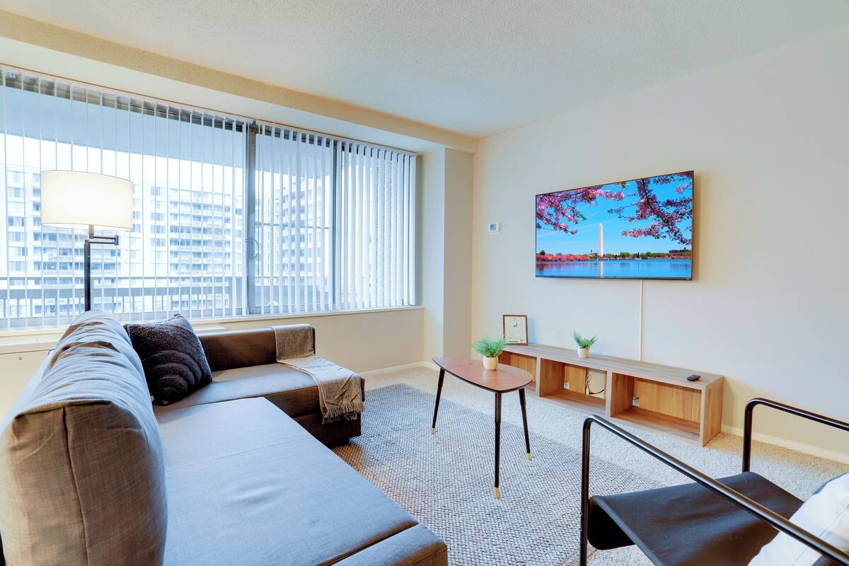 Een moderne woonkamer met een bank, een klein tafeltje en een aan de muur bevestigde televisie.