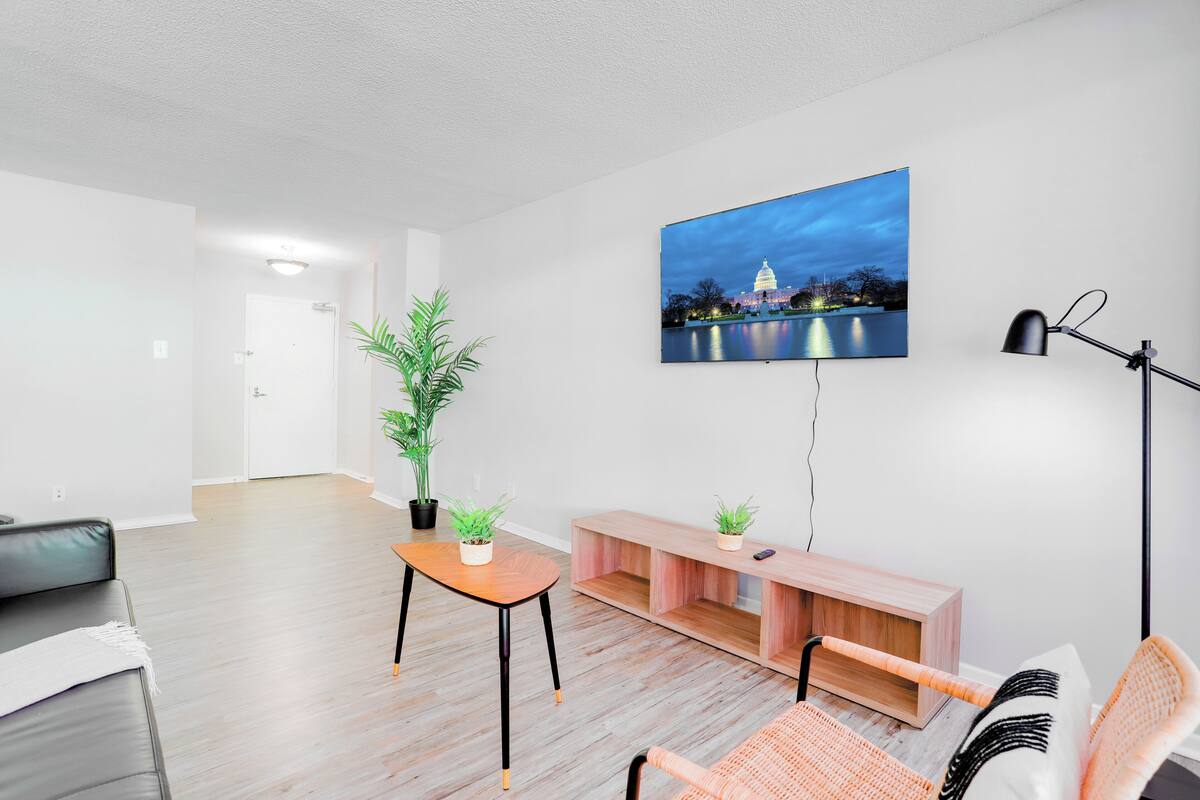 Een moderne woonkamer met een flatscreen televisie aan de muur, een houten salontafel, een bank, een fauteuil en een vloerlamp.