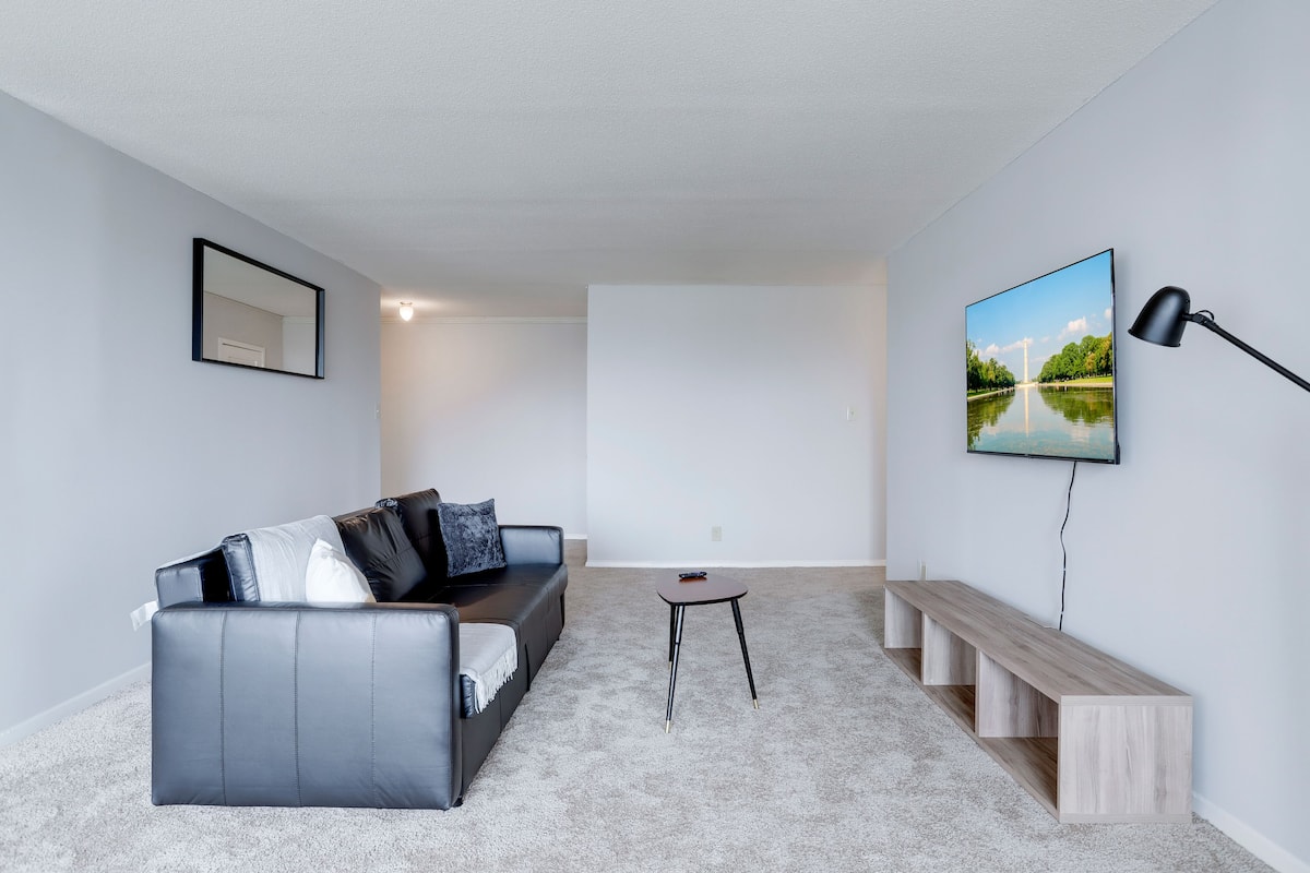 Een moderne woonkamer met een grijze bank, een kleine ronde tafel en een bankje.