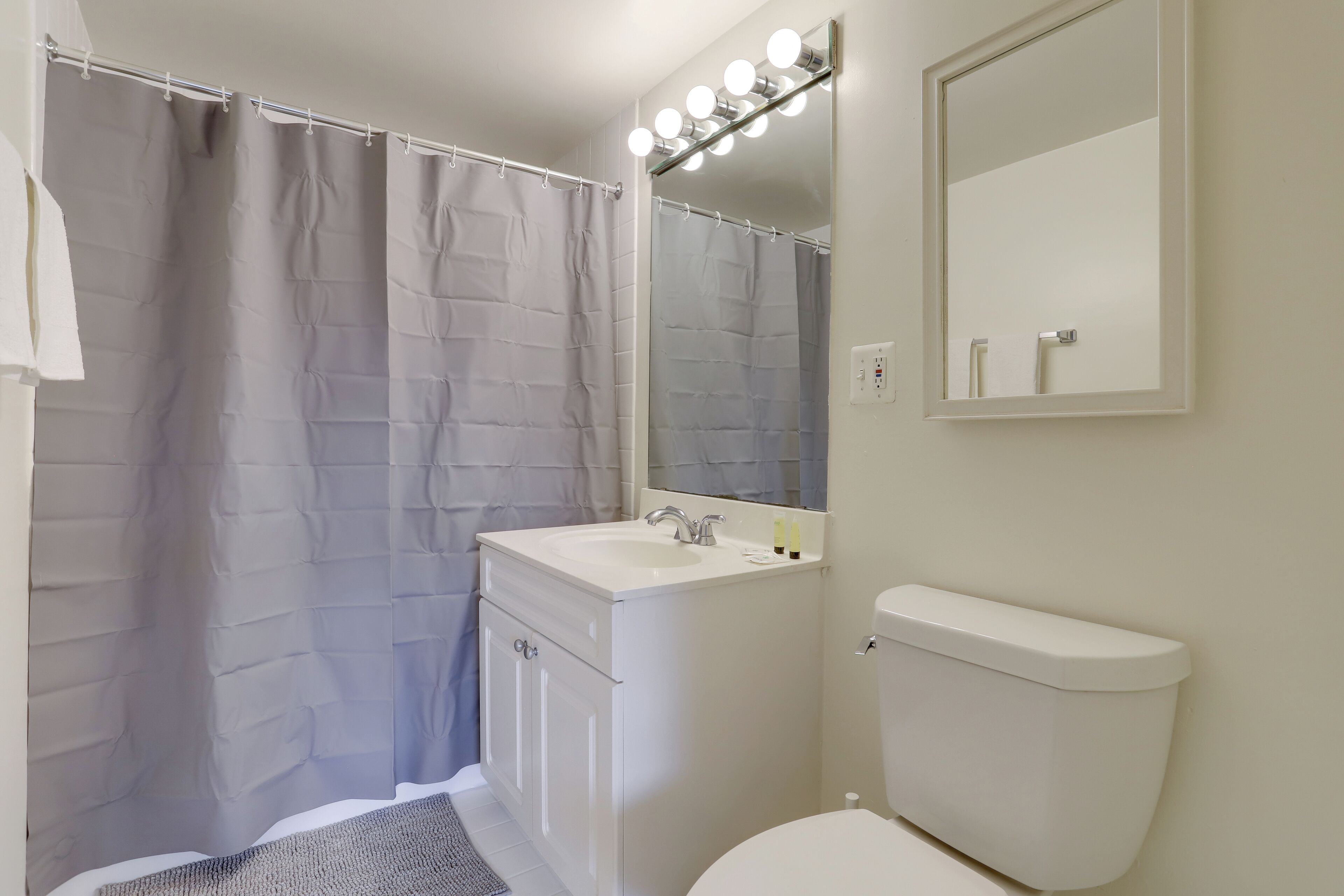 Un baño con cortina de ducha, lavamanos, espejo e inodoro.